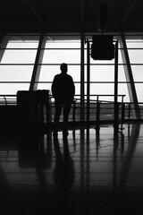 Black and white photograph of a man's silhouette in front of a large window at the airport.