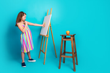 Young girl painting a still life on canvas in a bright room, focused on depicting a fruit on an art...