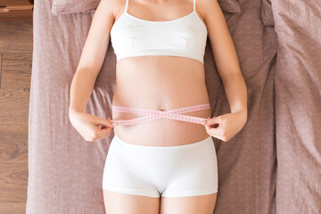 Young beautiful pregnant girl measuring her belly with a tape in home on bed. Healthy pregnancy...