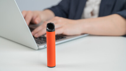 Caucasian businesswoman working on laptop. Disposable vape in foreground. 