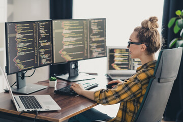 Young female programmer working remotely on multiple screens in a home office creating software...