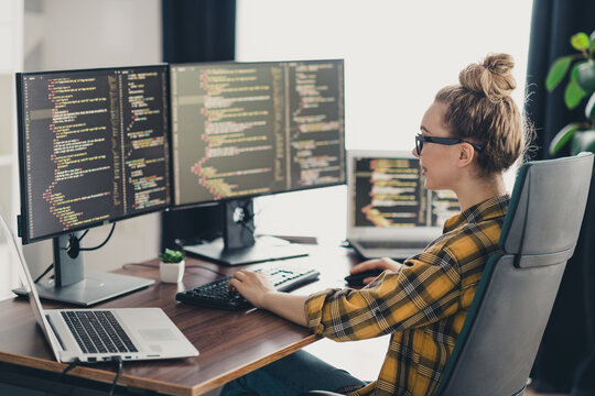Young female programmer working remotely on multiple screens in a home office creating software solutions with precision - Powered by Adobe