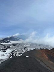 Majestic volcanic landscape featuring black lava rocks, snow-covered terrain, and billowing clouds...