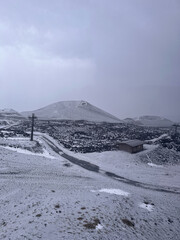 Snow-covered volcanic landscape with a winding road leading to a small building, surrounded by...