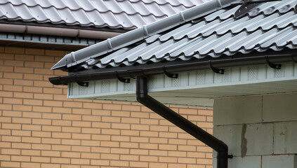 Roof with metal tiles and drainage system on a modern house in a residential area