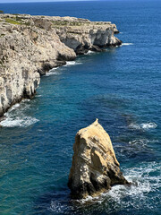 Coastal landscape featuring rugged cliffs and a solitary rock formation surrounded by clear blue...