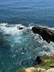 Scenic coastal view featuring rocky shoreline and vibrant turquoise waters, with gentle waves crashing against the rocks, creating a serene and picturesque natural landscape