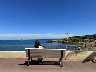 Woman with long hair sitting on a bench by the seaside, gazing at the tranquil ocean view under a...