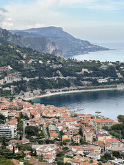 Obraz premium Scenic coastal view of a vibrant seaside town nestled between lush green hills and a serene blue bay, showcasing charming architecture and tranquil waters