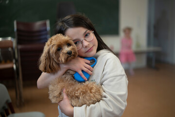 Smiling girl with glasses cuddling her dog at school. Concept: therapy animal, affection, calm in classroom, friendship and focus.