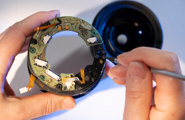 Camera lens repair process in a workshop with hands carefully fixing intricate components inside