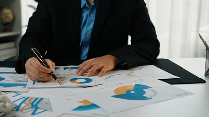 A business professional assesses various financial charts and reports on a tidy office desk,...
