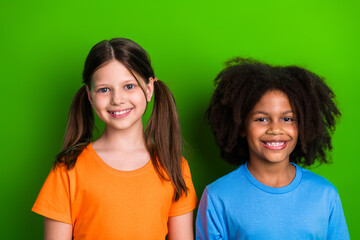 Smiling schoolgirls standing together against green background promoting friendship and diversity...