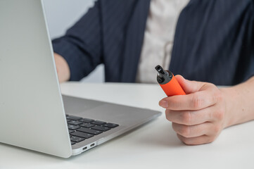 Faceless businesswoman smokes disposable vape and works on laptop. 