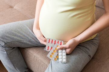 Midsection of pregnant woman taking vitamin pill on sofa at home