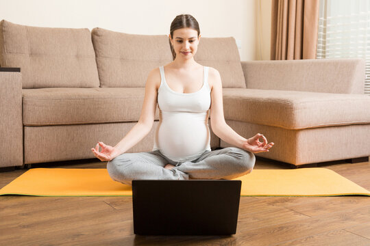 Young happy healthy yoga fitness beautiful pregnant woman doing bakasana yoga workout on yoga mat opposite laptop with online master class. lifestyle concept at coronavirus time - Powered by Adobe