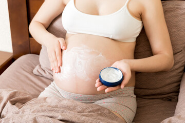 pregnant woman applying stretch mark cream to belly. pregnancy, people and maternity concept....