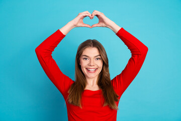 Joyful female in red making a heart gesture on blue background expressing love and happiness in a...