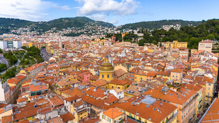 Aerial panorama of the historic Old Town of Nice, France, with vibrant rooftops and green hills in the background on a sunny day.