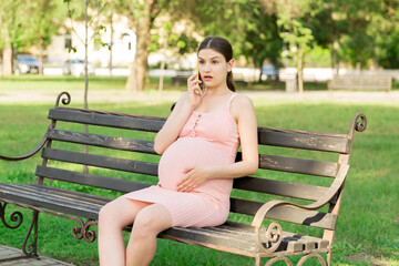 pregnant woman sits on a park bench and talking on phone