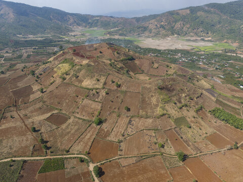 Aerial view of the terraced fields and sparse vegetation create a textured landscape under the vast sky, framing the distant mountains, Chu Pah, Gia Lai, Vietnam.