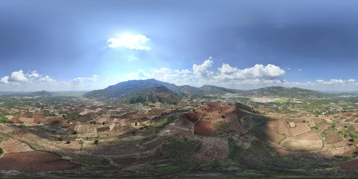 Aerial view of red soil agricultural plots contrasting with the verdant mountain ranges under a sky dotted with clouds, Chu Pah, Gia Lai, Vietnam.