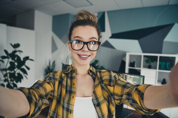 Young female freelancer with glasses smiling in cozy workspace wearing yellow plaid shirt in modern...