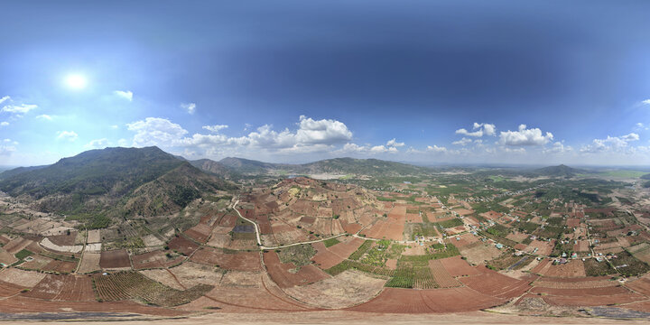 Aerial view of rich, red soil contrasting with the verdant mountains under a bright sky, Chu Pah, Gia Lai, Vietnam.