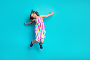 Cheerful young girl in a colorful dress against a teal background expressing fun and happiness through an energetic pose