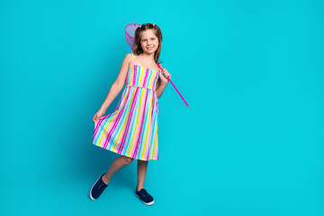 Adorable young girl in colorful striped summer dress posing cheerfully with a handheld net against...