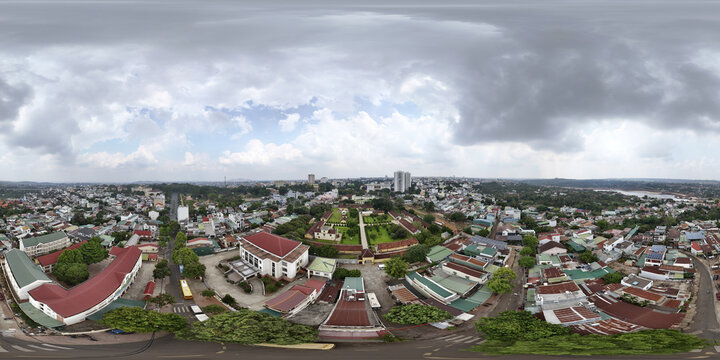 Aerial view of red-roofed buildings contrasting with lush greenery under a cloudy sky, showcasing urban architecture, Buon Ma Thuot, Dak Lak, Vietnam.