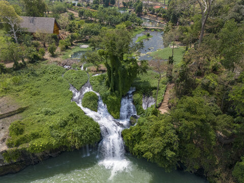 Aerial view of the Dray Nur Waterfall cascading into a turquoise pool, surrounded by vibrant green foliage and rustic structures, Buon Ma Thuot, Dak Lak, Vietnam.