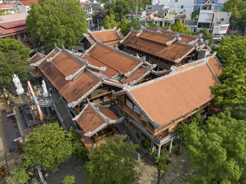 Aerial view of the intricate, multi-tiered Phap Vien Khai Doan Pagoda with its terracotta-tiled roofs nestled amidst lush green trees, Buon Ma Thuot, Dak Lak, Vietnam.