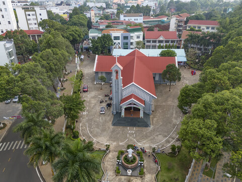 Aerial view of a red-roofed church stands majestically amidst lush green trees, its spire reaching towards the sky in a vibrant urban landscape, Buon Ma Thuot, Dak Lak, Vietnam.