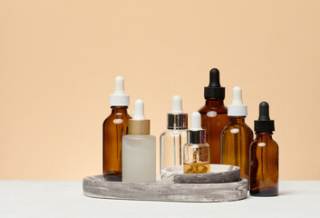 Various glass bottles with pipettes containing cosmetic serums or oils are arranged on a marble stand.