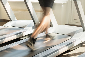 Person running energetically on treadmill in bright modern gym. Motion blur legs show speed and...