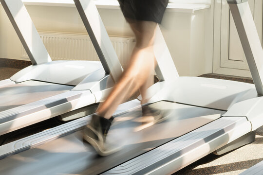 Person running energetically on treadmill in bright modern gym. Motion blur legs show speed and intensity. Workout session.