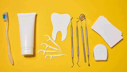White tube of toothpaste, toothbrush, dental instruments, plastic flossers, dental floss in cases and cut out on bright yellow background.