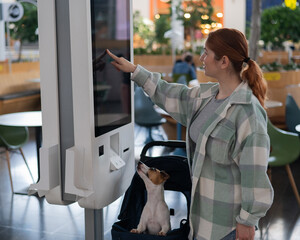 Caucasian woman makes a purchase at a self-service counter with a Jack Russell terrier dog in a...