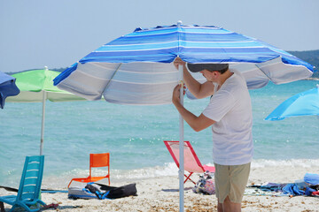 Young man setting up a beach umbrella on a sunny summer day. Travel, summer holidays, outdoor...