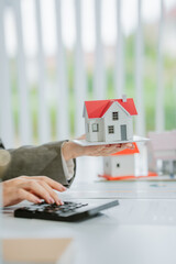 Close-up image of a male real estate agent holding a house model at his desk. property investment