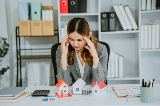 Asian businesswoman suffering from stress, fatigue, headache from working with bills, debts, insurance or loans. Real Estate Home Residential Consult about mortgage loan offerings in the office.
