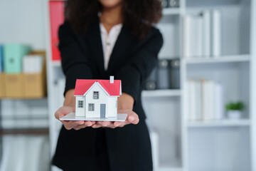 Confident American woman real estate agent stands proudly outside a modern home, radiating...