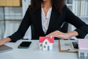 An African American female real estate agent presents a house model to a client, discussing...