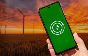 A male hand holding a smartphone with his right hand and a free energy concept and a wind turbine...