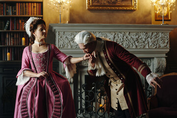 Caucasian middle aged man bowing and kissing hand of Caucasian middle aged woman wearing elaborate...