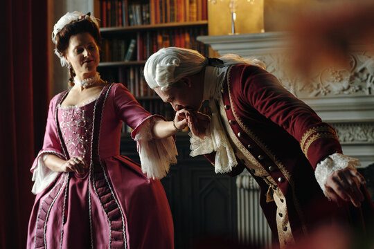 Caucasian middle aged man in historical Baroque costume bowing and kissing hand of Caucasian middle aged woman in Renaissance style dress