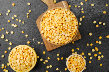 Multiple wooden bowls and spoon with yellow split peas on stone background for rustic meal prep,...