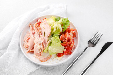 Protein salad with turkey, cheese and vegetables in white bowl with cutlery for fitness meal plan
