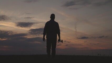 farming, silhouette of man walks with shovel in his hands across field against background of sunset...